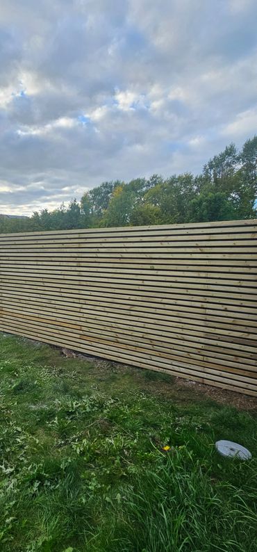 Newly built wooden fence with horizontal slats in a green yard.