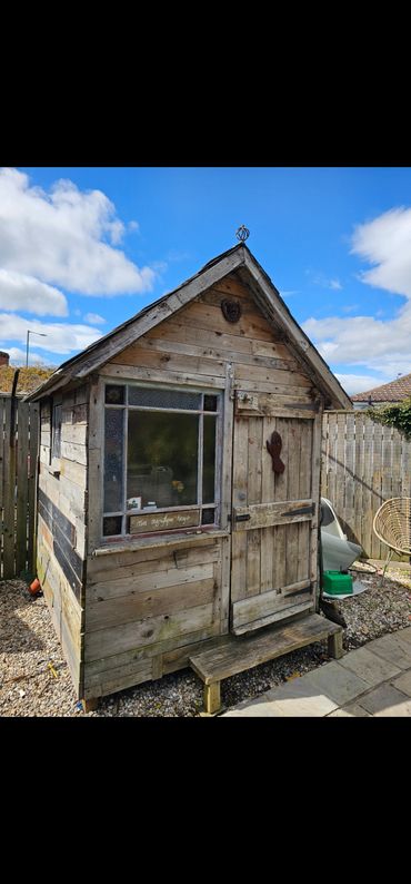Rustic wooden shed with a small bench outside under a blue sky.