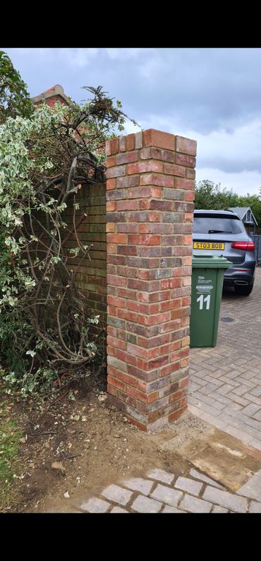 Newly built brick pillar next to a driveway with a green bin and car in the background.