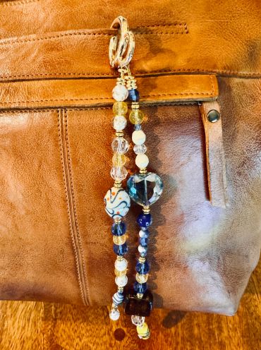 Beaded keychain with blue heart charm on leather bag.