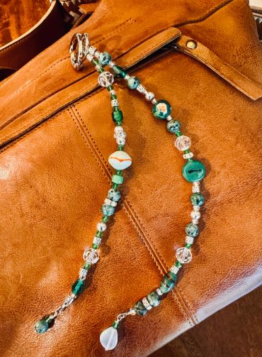 Green and silver beaded necklace on a brown leather surface.