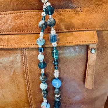 Blue bead keychain hanging on a brown leather bag.