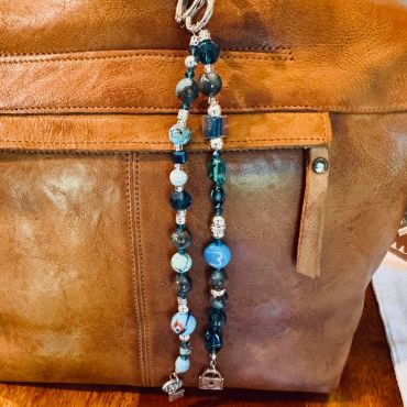 Blue beaded keychain with charms on a brown leather bag.