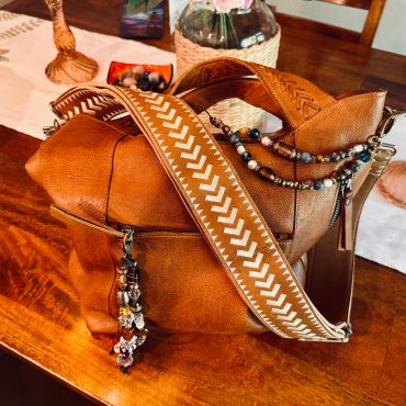 Close-up of a brown leather bag with a decorative patterned strap and bead necklace.