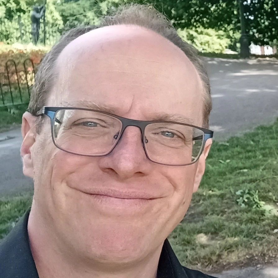 Smiling man wearing glasses outdoors in a park.