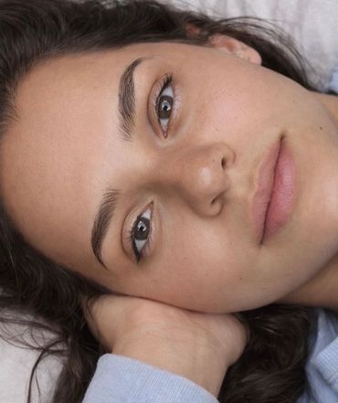 Close-up of a serene young woman lying down with her hand under her head.