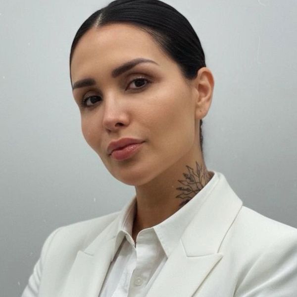Confident woman with sleek hair and neck tattoo in white blazer.