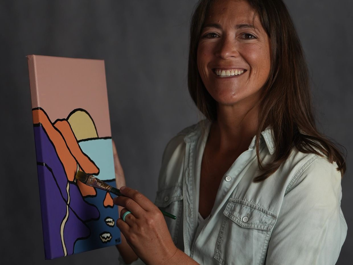 A smiling woman painting a colorful abstract landscape on canvas.