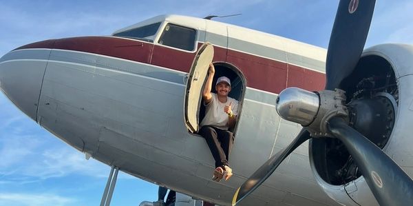 Person sitting in an open door of a vintage airplane.