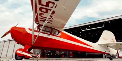 A red and white vintage airplane parked near a hangar.