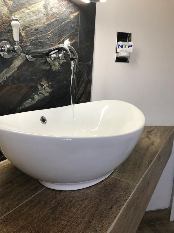 Water trickling from chrome wall mounted basin taps into countertop basin, sat on a floating worktop