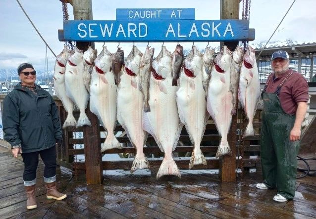 Two fishermen proudly display a large catch of halibut in Seward, Alaska.