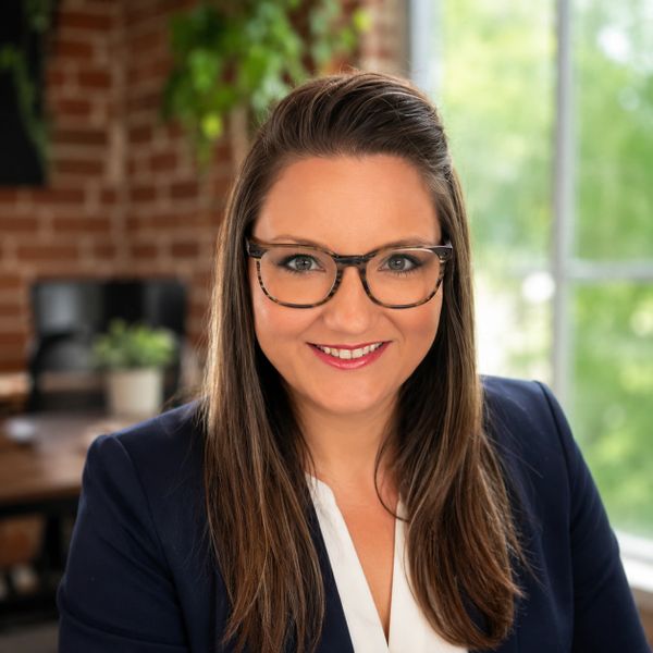 Professional woman with glasses smiling in a modern office setting.