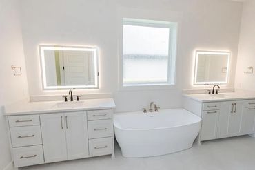 Modern white bathroom with illuminated mirrors and a central bathtub.