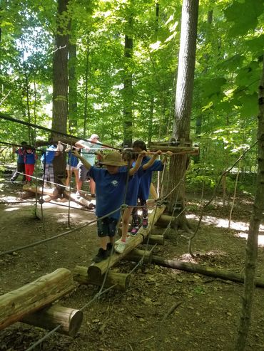 children walking on wooden planks while holding onto the rope side rails