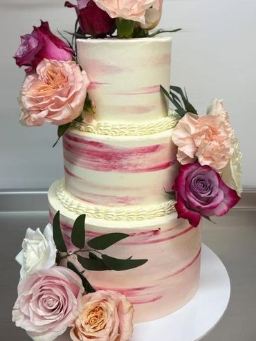 A beautiful 3 tier buttercream wedding cake with fresh flowers .