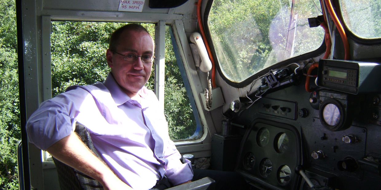 Man sitting in the driver's seat of a train cab with control panels.