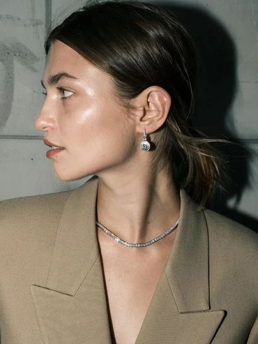 Profile of a woman wearing elegant earrings and a necklace with a beige blazer.
