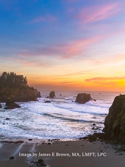 Coastal sunset with waves and rocky cliffs.