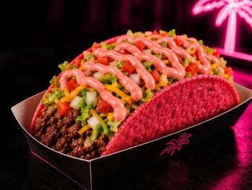 A colorful taco with pink shell, ground beef, lettuce, cheese, and pink sauce.