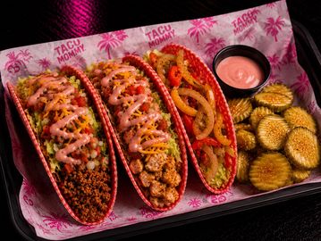 Three vibrant tacos with sides of fried pickles and dipping sauce on branded paper.