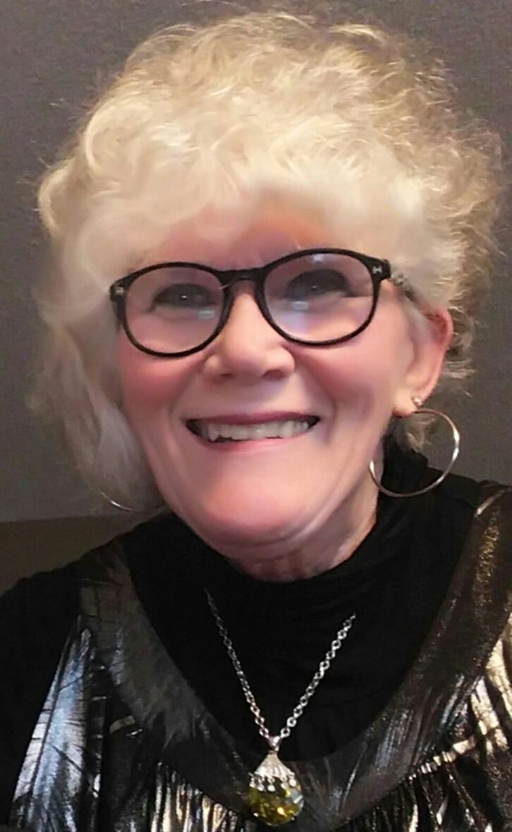 Smiling elderly woman with curly white hair and glasses.