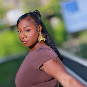 Confident woman with sleek hairstyle and gold earrings posing outdoors.