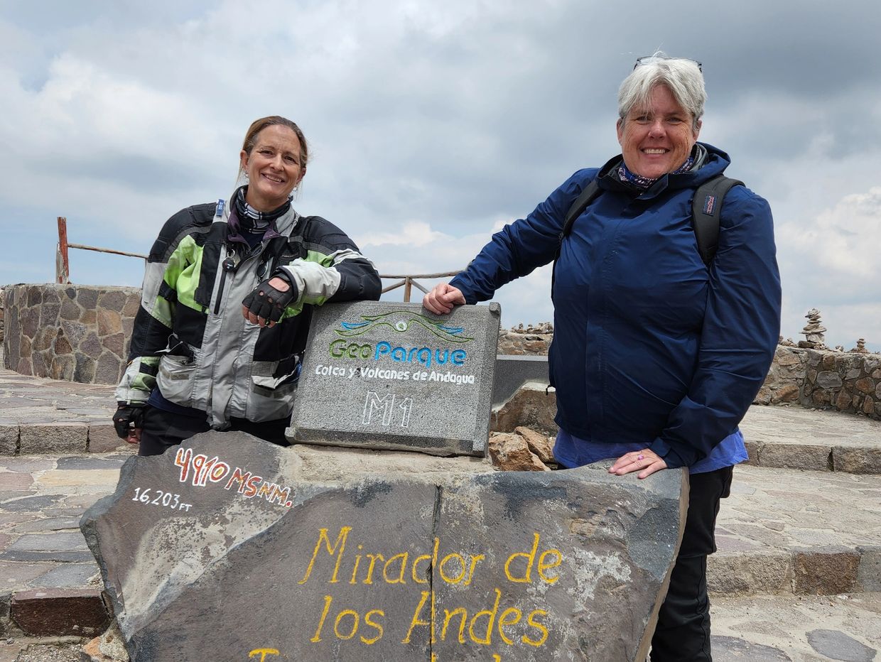 Two women smiling at Mirador de los Andes sign at GeoParque Colca y Volcanes de Andagua.