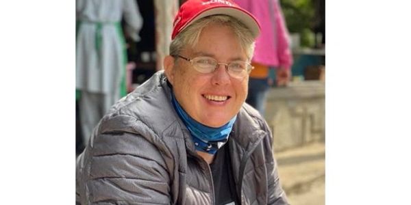 Smiling person wearing glasses, a red cap, and a gray jacket outdoors.
