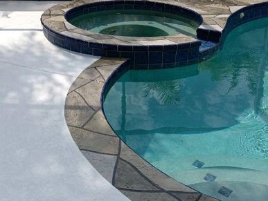 Curved pool with a hot tub and stone border.