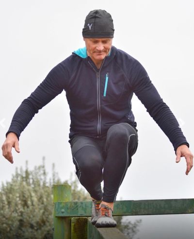 Man in athletic wear balancing on a green metal beam outdoors.