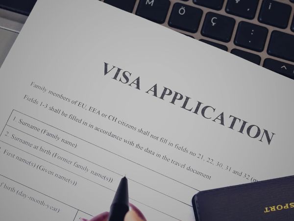 Person filling out a visa application form beside a passport on a laptop.