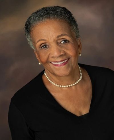 Smiling elderly woman wearing pearls and a black top.
