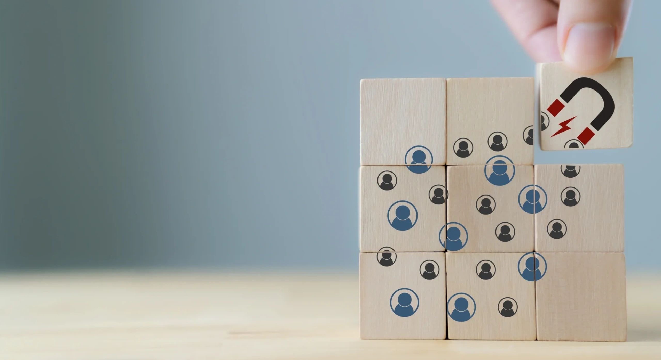 Hand placing a wooden block with a magnet symbol among blocks with people icons.