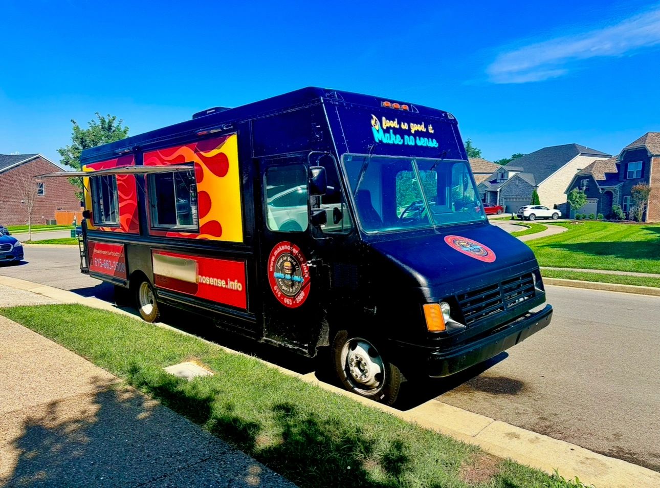 Black food truck with red and yellow flame design parked on a residential street.