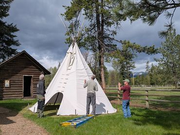 three people setting up a top, ladder on grass