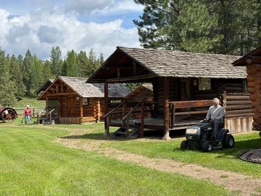 man mowing grass near log cabins