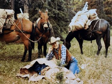 man wearing cowboy hat, two horses in background