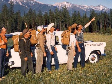 men standing in front of research and rescue vehicle, mountains in background