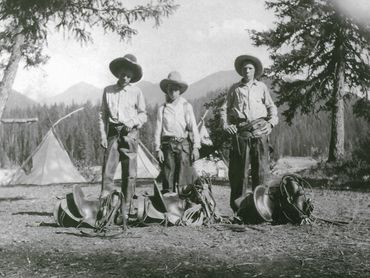three cowboys with saddles, tents in background
