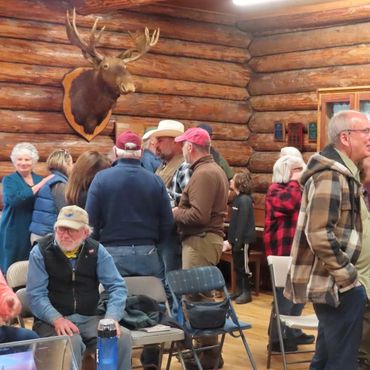 group of people, in log building room, moose head hanging on wall