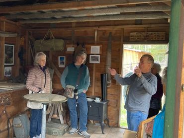 man speaking to two women inside historic log cabin