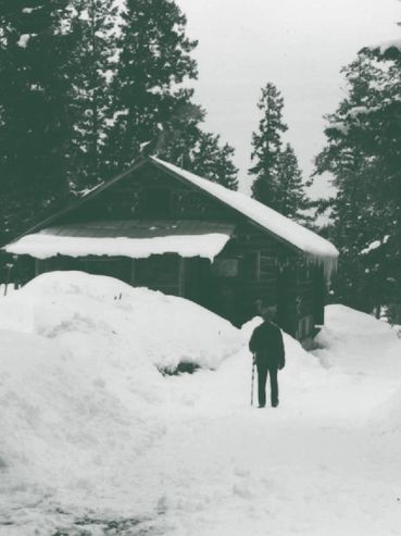 man walking on path in snow, cabin in background