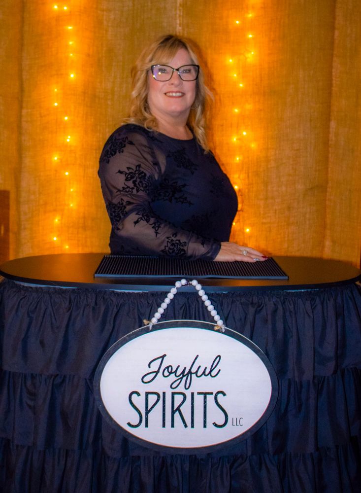 Woman stands behind a table with a sign reading "Joyful Spirits LLC."