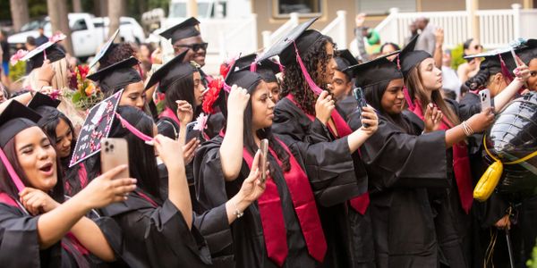 Graduates in caps and gowns capturing their celebration on phones.