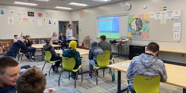 Students attentively listen to a teacher presenting in a classroom.