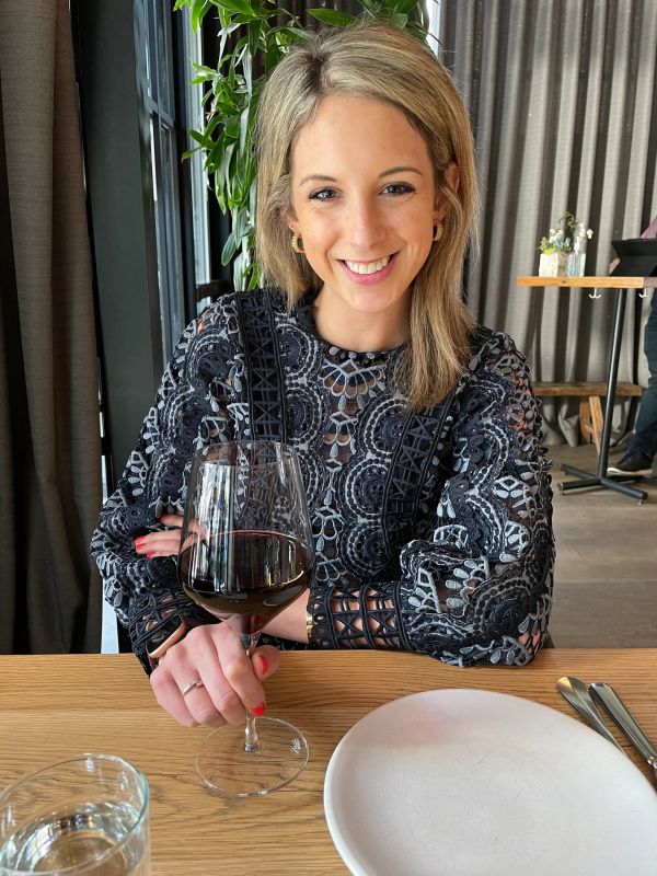 Smiling woman holding a glass of red wine at a restaurant table.