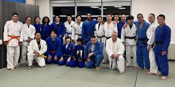 Group of judo practitioners posing together in a dojo, wearing blue and white gis.