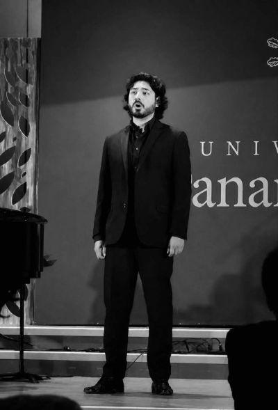 Hombre cantando en un escenario con traje negro.