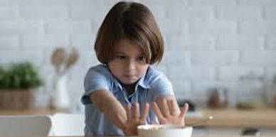 A child stretching hands towards a bowl of cereal on the table.